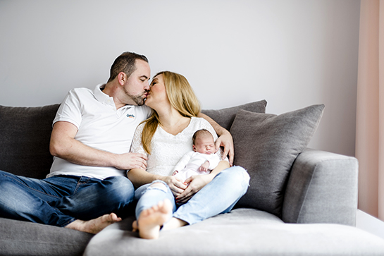 Fotograf Münster: Beispiel für Familienbild: Knutschendes Pärchen mit schlafendem Baby auf dem Schoß