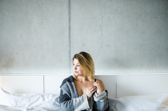 Fotograf Münster: Vorschaubild für Aktfotos mit Dame, die leicht bekleidet auf dem Bett sitzt und sich durch die Haare streicht.